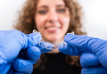 Orthodontist doctor in gloves holding silicone invisible transparent braces show to woman in dental clinic. Happy girl with correcting teeth. Treatment and cure in dentistry.