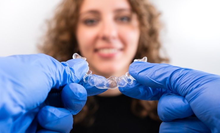 Orthodontist doctor in gloves holding silicone invisible transparent braces show to woman in dental clinic. Happy girl with correcting teeth. Treatment and cure in dentistry.