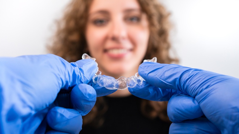 Orthodontist doctor in gloves holding silicone invisible transparent braces show to woman in dental clinic. Happy girl with correcting teeth. Treatment and cure in dentistry.