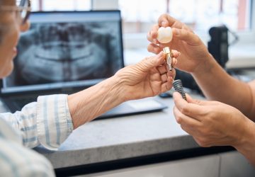 Dentist showing a senior patient a dental implant, abutment and crown during a consultation about whether All-on-4 implants are removable