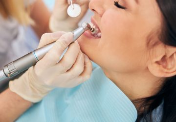 Dental hygienist using a polishing handpiece and mouth mirror during a dental cleaning for a relaxed female patient