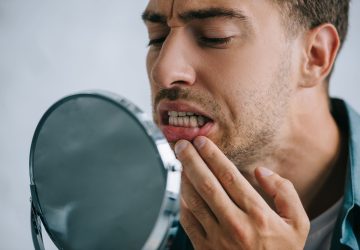 Man looking in a mirror and pulling down his lower lip to check his gums for signs of a tooth abscess