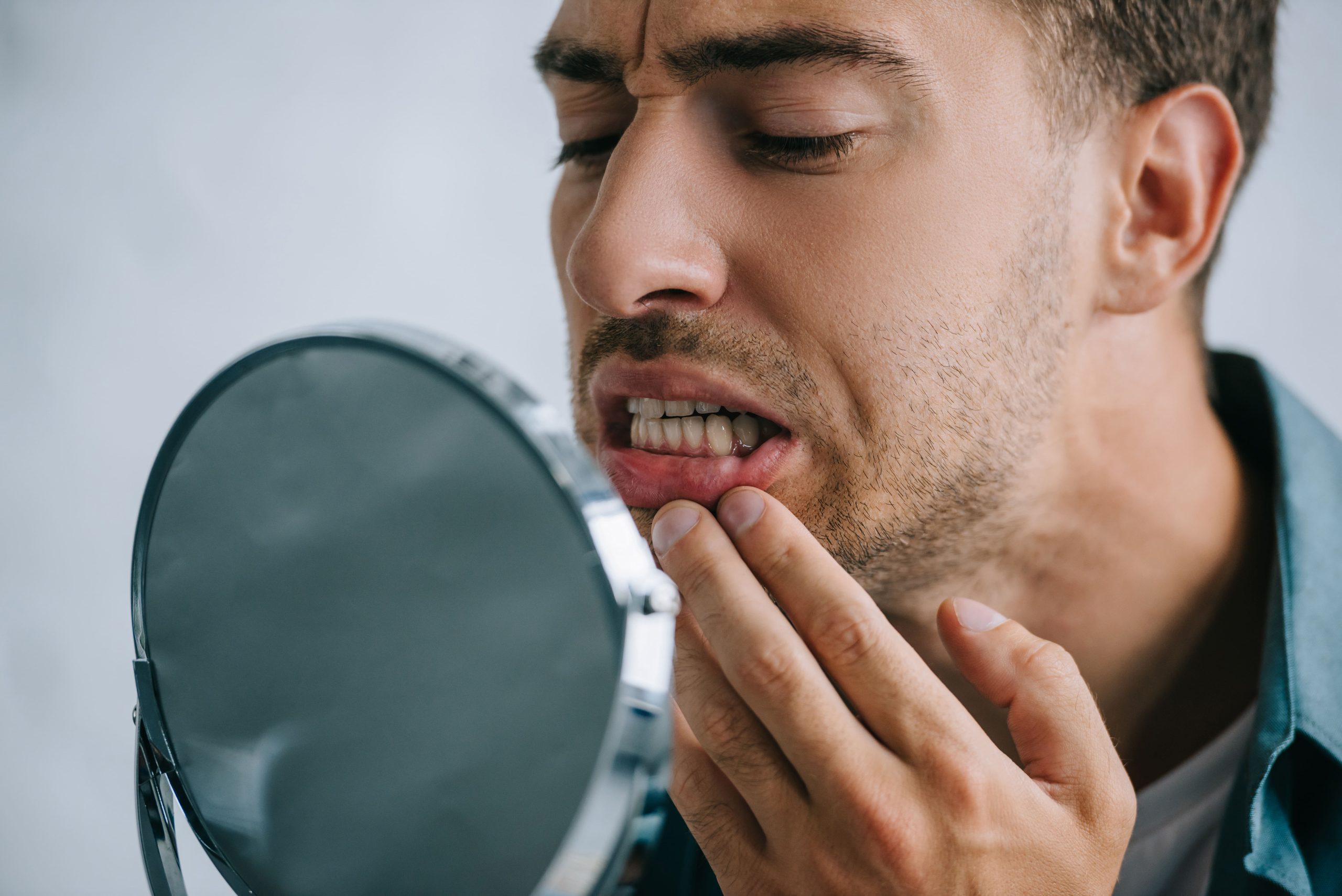 Man looking in a mirror and pulling down his lower lip to check his gums for signs of a tooth abscess