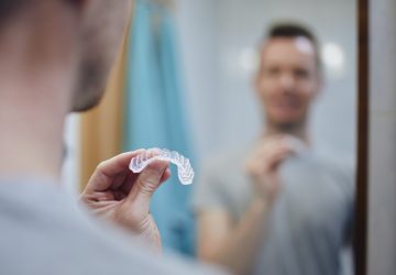 Man holding a clear custom night guard used for teeth grinding treatment in front of a bathroom mirror